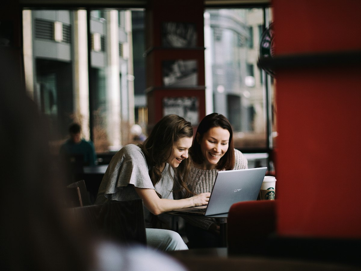 Two women looking at a laptop together in a café